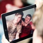 Auf diesem Bild sieht man ein Tablet. Ein Junge fotografiert mit dem Tablet zwei andere Jungen. Ein Junge benutzt die Gebärde für das Wort Handy.